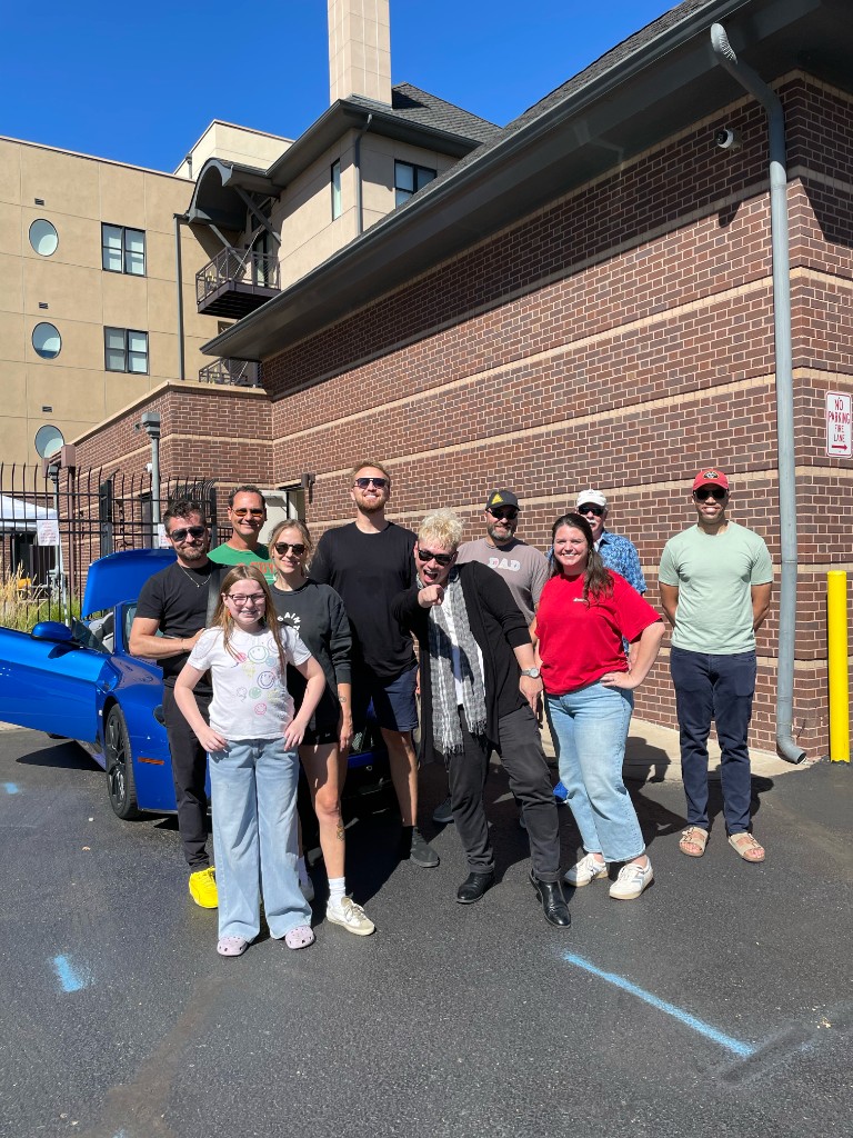 Cars & Kids group photo beside a blue sports car