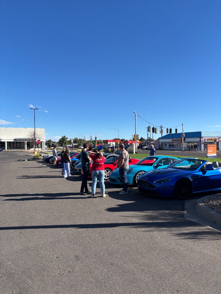 People standing with a row of sports cars in a parking lot