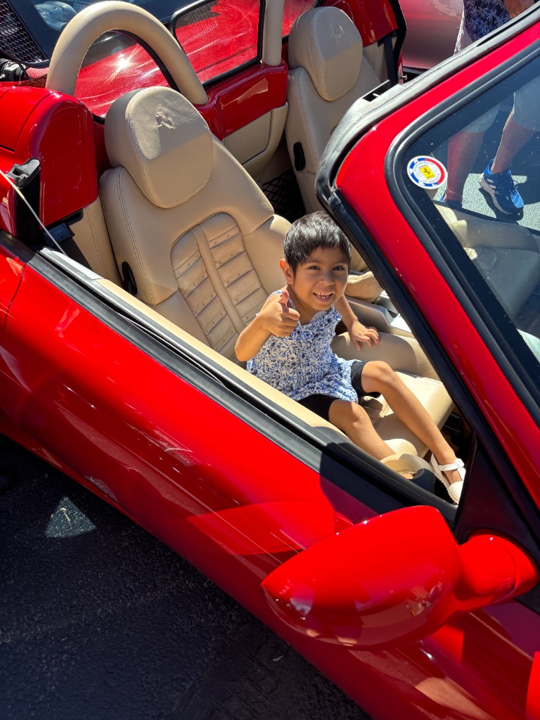 Child giving a thumbs-up from the seat of a red convertible