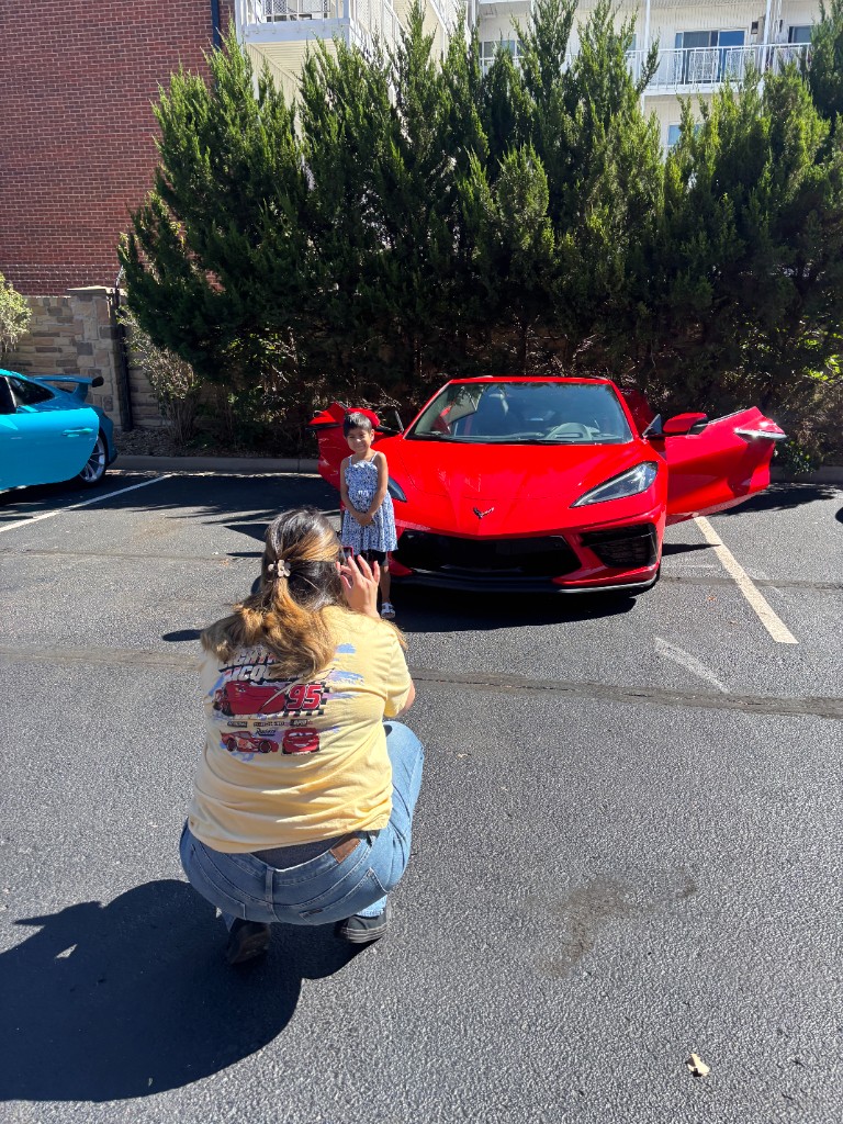 Adult kneeling to photograph a child in front of a red Corvette