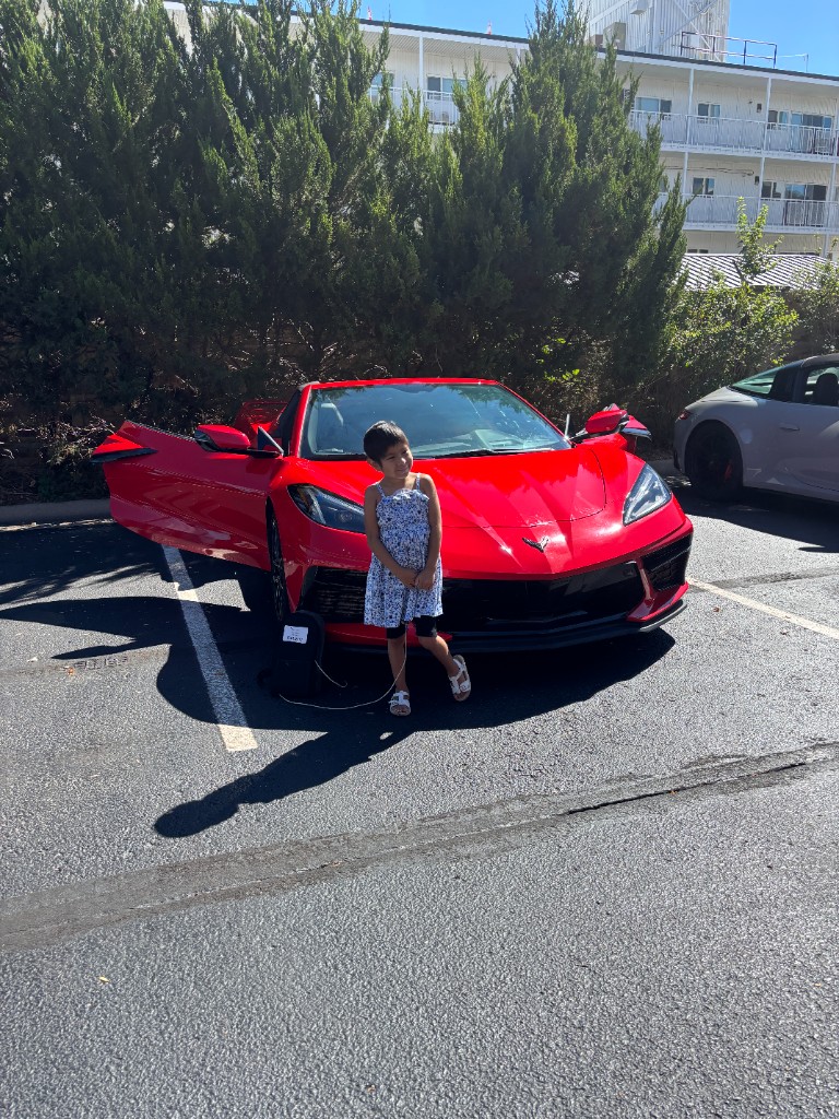 Child standing in front of a red Corvette with both doors open