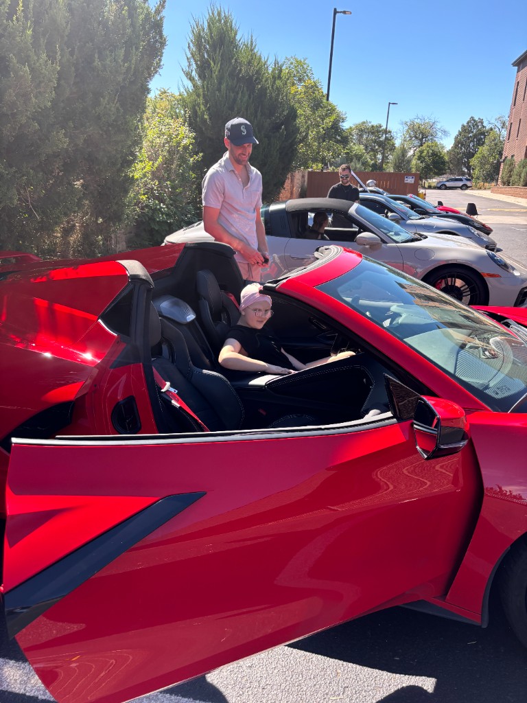 Child in a pink cap sitting in a red Corvette with the door open