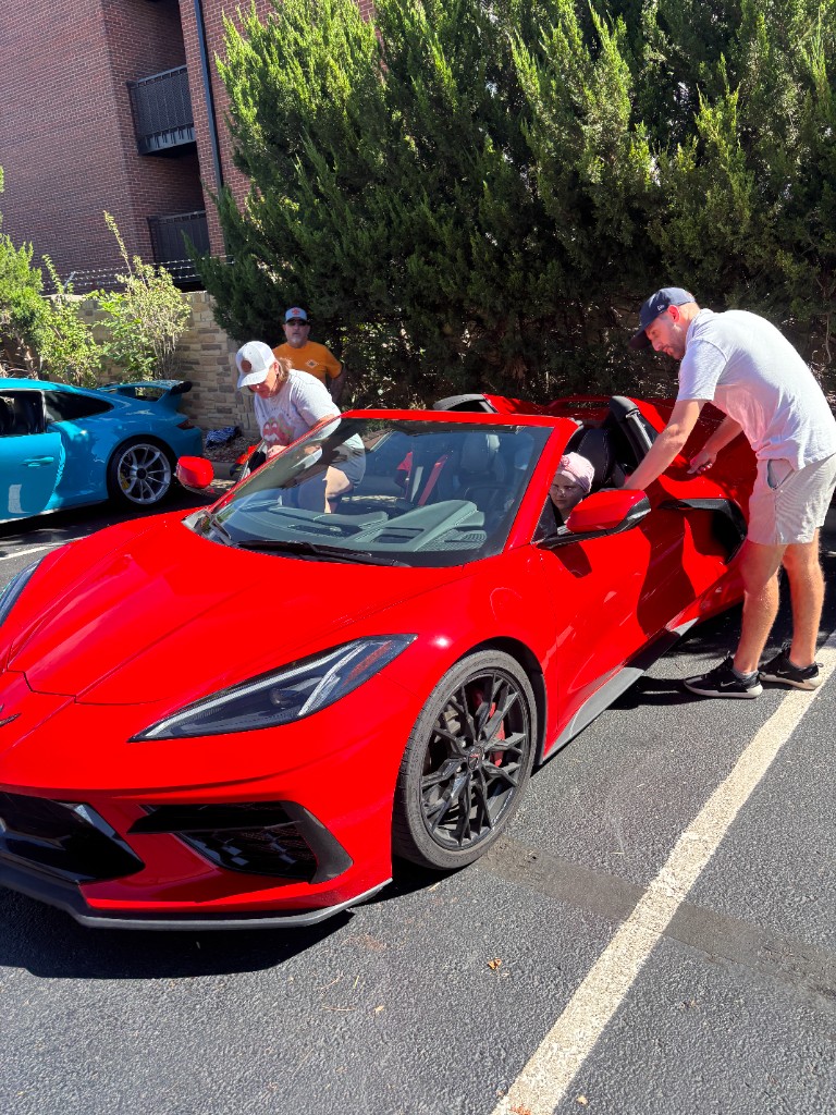 Red Corvette with the door open and people gathered around it