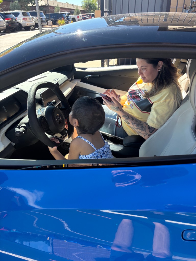 Child at the wheel of a blue sports car while an adult sits beside them